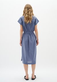 Rochie din in albastru cu mâneci scurte, talie strânsă și design de lungime medie. Are un model texturat și slituri laterale pentru ușurința mișcării.