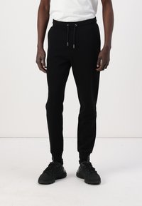 Zwarte sweatpants van zacht materiaal, met een elastische tailleband met koordjes, taps toelopende benen en ribbels aan de boorden.