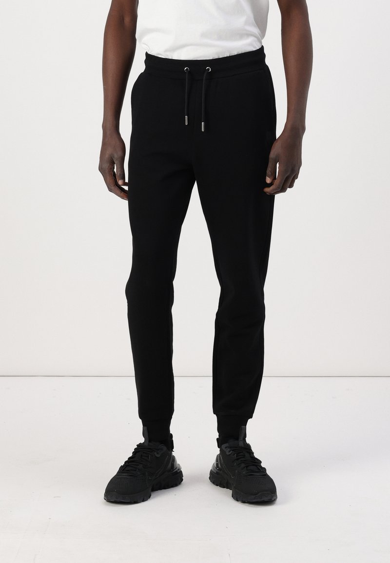 Zwarte sweatpants van zacht materiaal, met een elastische tailleband met koordjes, taps toelopende benen en ribbels aan de boorden.