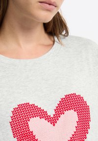 Camicetta grigia a maniche corte con un design a forma di cuore rosso con dettagli rosa al centro. Tessuto morbido con colletto girocollo classico.