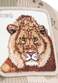 Casquette en velours côtelé avec un visage de lion brodé sur une pièce de tissu clair, présentant des textures de fourrure détaillées et des yeux jaunes éclatants.