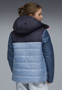 Gepolsterte Jacke mit einem navyblauen und hellblauen Farbblockdesign, abnehmbarer Kapuze und horizontaler Stepptextur.