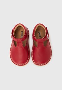 Ζευγάρι κόκκινων παιδικών δερμάτινων παπουτσιών Μαίρη Τζέιν με κυμματιστές άκρες και λουράκια με ασημένιο πόρπη σε λευκό φόντο.