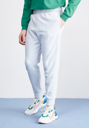 Hellblaue Jogginghosen aus einem weichen Baumwollmix, mit seitlichen Taschen und gesticktem Logo. Getragen mit bunten Sportschuhen.