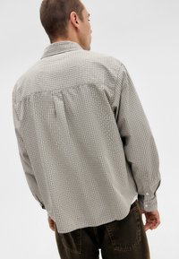 Checkered button-up shirt in light gray and dark gray, featuring long sleeves and a back yoke design. Soft cotton fabric with a relaxed fit.