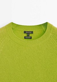 Pull en cachemire vert avec un col rond, des bordures côtelées et une texture lisse. L'étiquette indique "100 % cachemire, fabriqué en Chine."