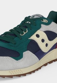Baskets avec lacets et parties vert foncé, sections en mesh bleu marine, surpiqûres en suède gris, écusson logo blanc et semelle beige avec empreinte marron.