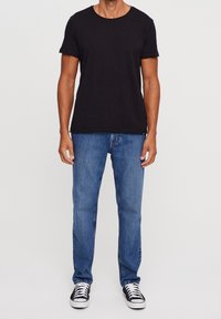 Svart t-shirt med kort ärm i mjuk bomull, kombinerad med ljusblå raka jeans och svarta och vita sneakers. Enkel design.