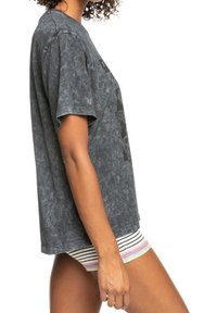 Camiseta gris de gran tamaño con un acabado de lavado mineral, con mangas cortas y un corte holgado. Llevada con pantalones cortos a rayas por debajo.