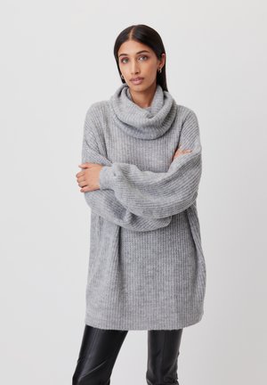 Light grey oversized sweater with a cowl neck, textured knit fabric, long sleeves, and a relaxed fit, paired with black leather pants.