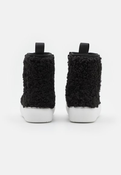 Sapatos de cano alto com textura de pelo preto e solas de borracha branca, apresentando uma aba traseira para facilitar o calce. Design limpo e minimalista.