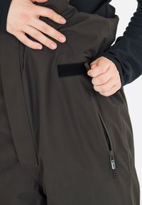 Svart ytterklädsel med en slät yta, som har en sidoficka med dragkedja och ett kardborrestängning. Tyget verkar vara vattenavvisande och hållbart.