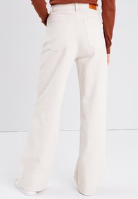 Hvide højtaljede vide jeans lavet af denim, med baglommer, et brunt mærke og en ren finish i kanten.