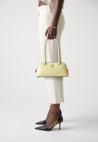 Żółta skórzana torebka o zaokrąglonym kształcie, czarne akcenty i zamek błyskawiczny. Noszona z białymi, skróconymi spodniami i czarnymi szpilkami o zaostrzonych czubkach.