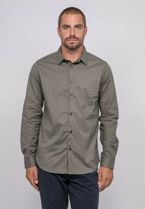Chemise boutonnée vert olive avec un motif géométrique subtil, manches longues et boutons foncés. Présente un col pointu et une coupe ajustée.