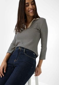 Maglietta a maniche lunghe a righe in navy e crema, con scollatura a V e colletto a contrasto, abbinata a jeans blu scuro con accenti rame.