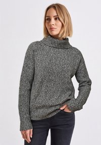 Grauer gestrickter Pullover mit hohem Schlauchkragen, strukturiertem Muster und leicht oversized Passform, kombiniert mit dunkler Hose.