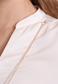 Rosa blus med en slät textur, prydd med en delikat guldkedja som är fäst vid halsringningen för extra detalj.