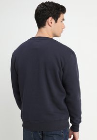 Felpa blu navy in cotone con collo rotondo, polsini e vita a costine. Caratterizzata da un'etichetta sul retro e vestibilità classica.