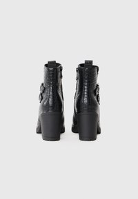 Black heeled ankle boots with a crocodile texture, two adjustable straps, rear zippers, and a sturdy, chunky heel.
