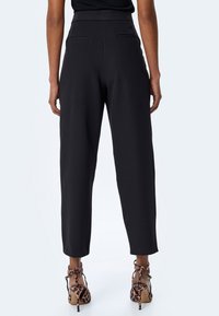 Czarne spodnie z wysokim stanem o luźnym kroju, z dwoma tylnymi kieszeniami, zestawione z leopardzimi butami na obcasie.