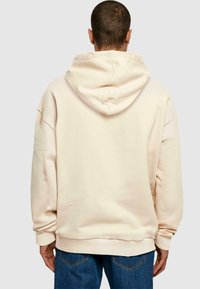 Sudadera de gran tamaño color crema con capucha ajustable, hombros caídos y puños acanalados. Textura de tela suave y corte relajado.