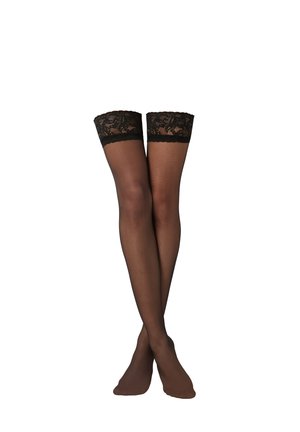 Černé průsvitné samodržky s krajkovými lemy, nošené na zkřížených nohách na bílém pozadí.