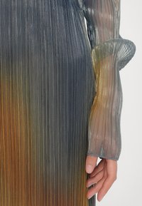 Durchsichtiges, plissiertes Kleid mit einem Farbverlauf von Dunkelgrau zu Orange. Lange, durchsichtige Ärmel mit einem Manschettendetail.