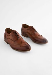 Ruske nahkakenkäparit, joissa on klassinen brogue-muotoilu, porareikäkoristelu, teräväkärkinen muoto ja matala pinottu korko.