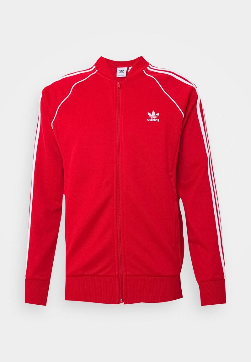 Röd zip-up träningsjacka i mjukt material, med vita randiga detaljer längs axlarna och armarna samt en broderad logotyp på bröstet.