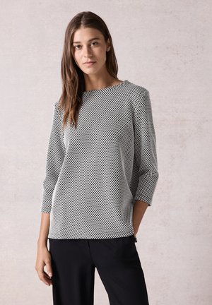 Zwart-witte blouse met stippen, een ronde halslijn, driekwartmouwen en een losse pasvorm, gecombineerd met zwarte broek.
