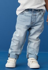Jean en denim délavé avec des poignets retroussés, présentant une coupe décontractée et des coutures contrastées. Associés à des baskets blanches à velcro.