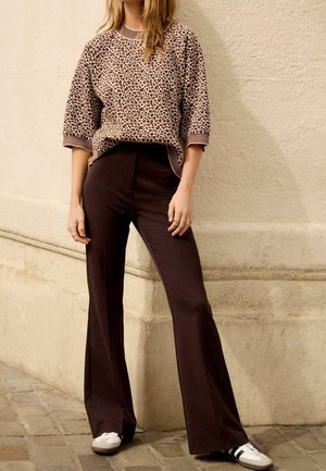 Haut à manches courtes en imprimé léopard, avec des poignets côtelés marron, associé à un pantalon évasé sombre et des baskets blanches avec des rayures noires.