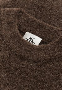 Bruin wollen trui met een zachte, fuzzy textuur. Heeft een brede halslijn en een wit label met een zwart logo dat aan de binnenkant is genaaid.