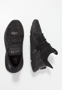 Black athletic shoes with a textured mesh upper, padded tongue, and rubber sole featuring geometric patterns for grip.