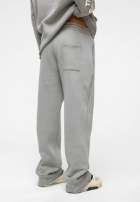 Grijze sweatpants van zacht materiaal, met een achterzak, relaxte pasvorm en geribde boorden. Voorkant en zijnaad zijn zichtbaar.