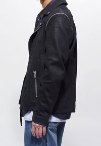 Černá kožená moto bunda s přiléhavým střihem, stříbrnými zipy a cvočky, texturovaným povrchem a bočními kapsami.