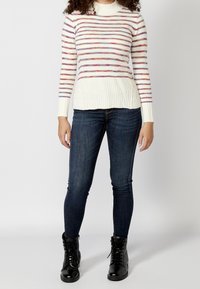 Pull rayé crème, rose et bleu, avec un ourlet côtelé et un col montant, associé à un jean skinny foncé et des bottes noires à lacets.