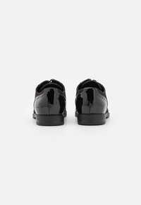 Chaussures en cuir verni noir avec une texture lisse, une forme arrondie et un petit talon. Présentent des coutures discrètes et un design classique.