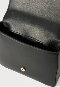 Sac en cuir noir avec une surface texturée, de forme rectangulaire, fermeture à pression dorée et un intérieur simple non doublé.