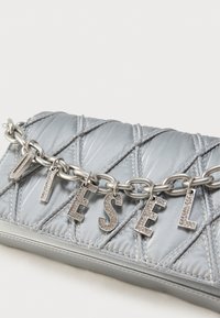 Sac à main argenté matelassé avec une chaîne brillante formant les lettres « DIESEL », et une base en cuir lisse avec des coutures décoratives.