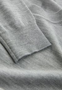 Grå sweaterdetalje, der viser en blød, strikket tekstur. Mansjetten har et rent finish med en let mørkere grå tone, der smelter sammen med stoffet.