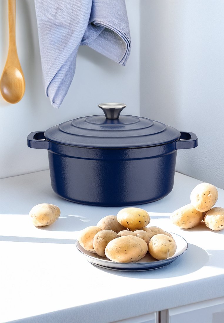 Faitout en fonte bleu marine avec un couvercle strié, un bouton en argent et des poignées latérales. Entouré de pommes de terre crues sur une assiette et d'une cuillère en bois.