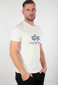Beige t-shirt lavet af bomuld, med et sort logo og geometriske designs. Korte ærmer, rund halsudskæring og en slim fit.