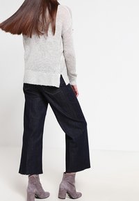 Vaaleanharmaa neulottu neule, jossa on sivuhalkiot, yhdistetty tummansinisiin leveälahkeisiin farkkuihin ja harmaisiin nilkka-saappaisiin. Sileä pinta ja rento istuvuus.