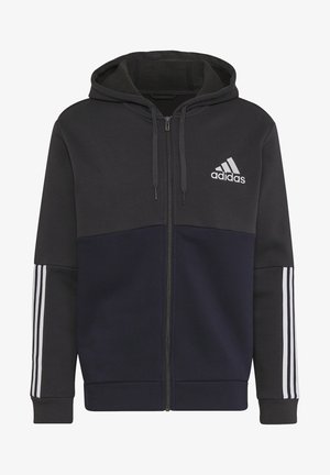 Mann trägt einen schwarzen und dunkelblauen Adidas Reißverschluss-Hoodie mit drei weißen Streifen an den Ärmeln und passenden dunkelblauen Hosen.