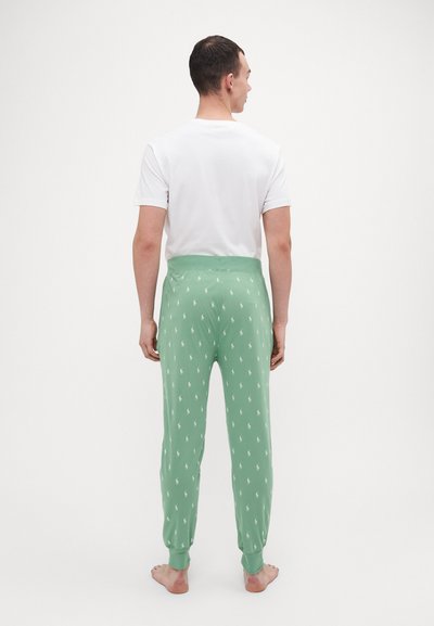 Pantalons de pyjama verts avec un motif de logo de cheval blanc, taille élastique, poignets fuselés et tissu léger, associés à une chemise blanche.