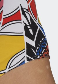 Mönstrad baddräktstyg i färgglada nyanser med djärva geometriska mönster i rött, gult, svart och blått. Slät textur med kontrasterande detaljer.