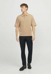 Beige polo shirt with vertical ribbed texture, short sleeves, and three buttons. Paired with dark blue pants and black slip-on shoes.