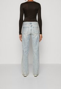 Jeans a campana di colore blu chiaro con decorazioni in strass e tasche posteriori classiche, abbinati a un top nero a maniche lunghe.